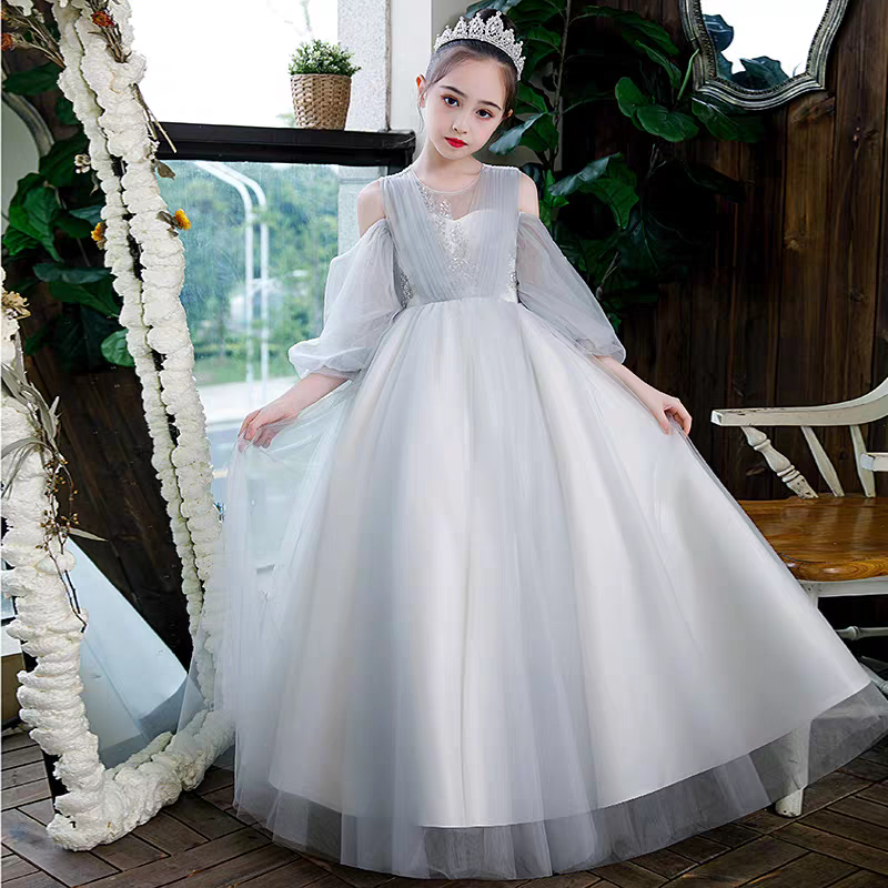 Girl in a light grey formal dress with sheer sleeves and a tiara, holding the skirt.