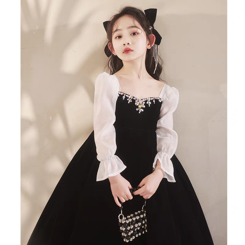 Girl in black velvet dress with white sleeves and gem detailing holding beaded purse.