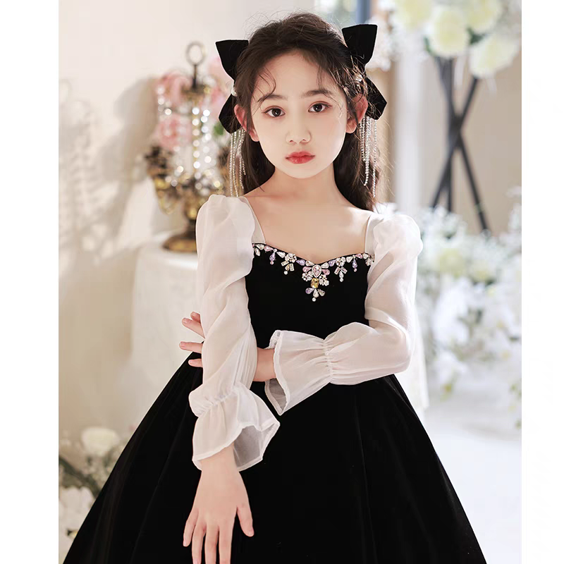 Girl in black velvet dress with sheer sleeves and jewel neckline, wearing bow headband.