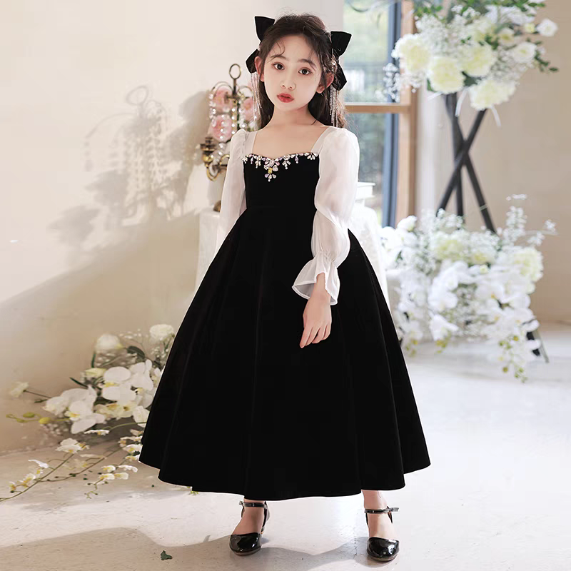 Girl in black velvet dress with sheer sleeves and jewel neckline, wearing black shoes and hair bow.