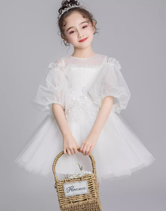 Girl in white tulle dress with sheer sleeves and floral detail, holding flower basket.