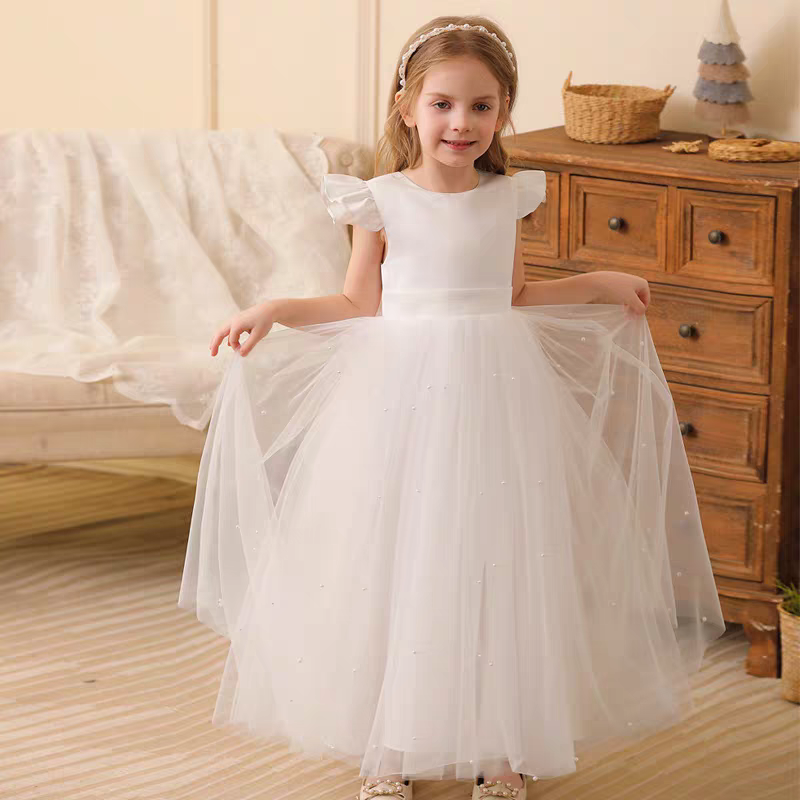 Girl wearing a white tulle flower girl dress with pearl accents and a matching headband.