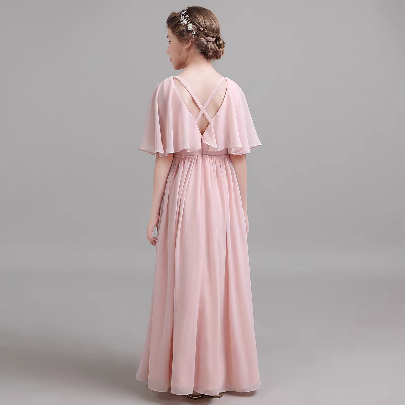 Back view of a girl wearing a pink chiffon formal dress with cape sleeves and criss-cross straps.
