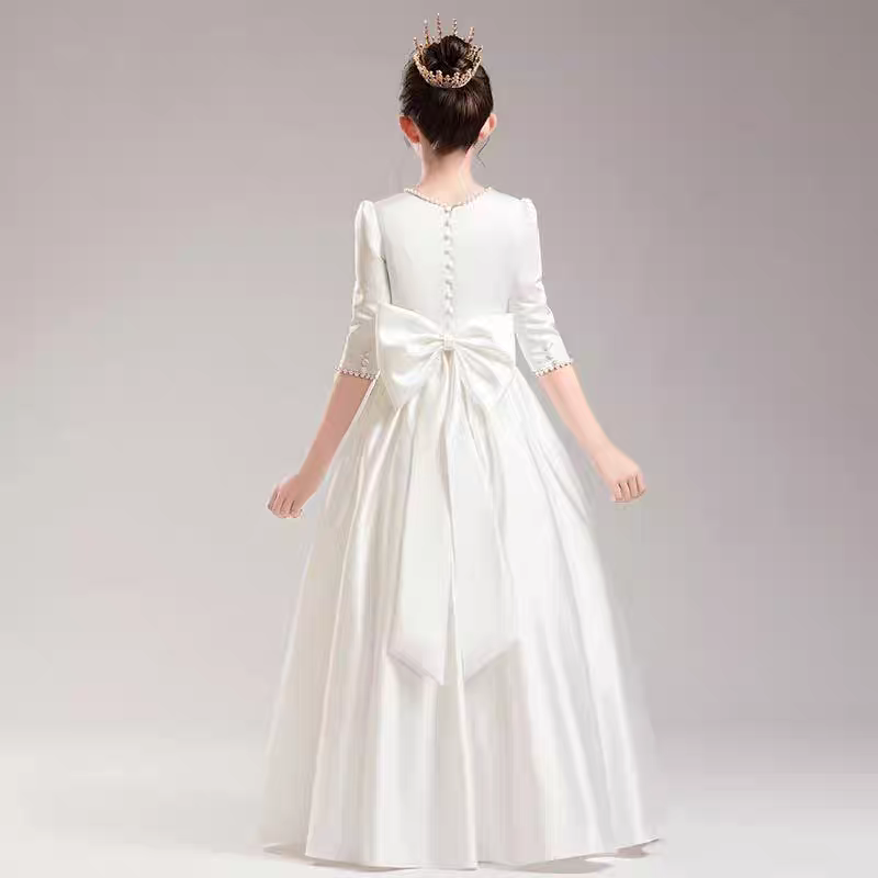 Back view of girl in white satin gown with large bow and small crown. Formal wear for kids.