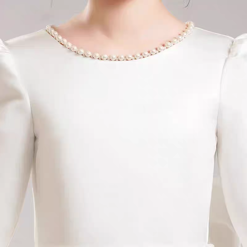 Close-up of a white dress with pearl-lined neckline and puff sleeves.