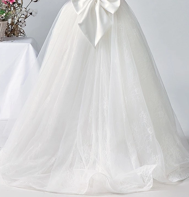 Close-up of a white lace wedding dress with tulle overlay and large satin bow.
