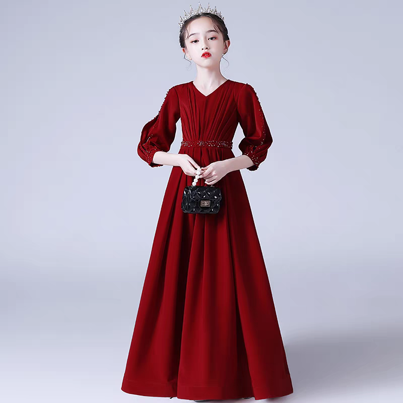 Girl in red velvet formal gown with balloon sleeves, embellished belt, and crown, holding a black purse.