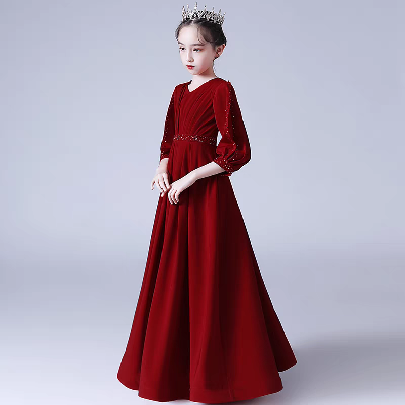 Girl in red velvet gown with beaded sleeves and belt, wearing a crown.