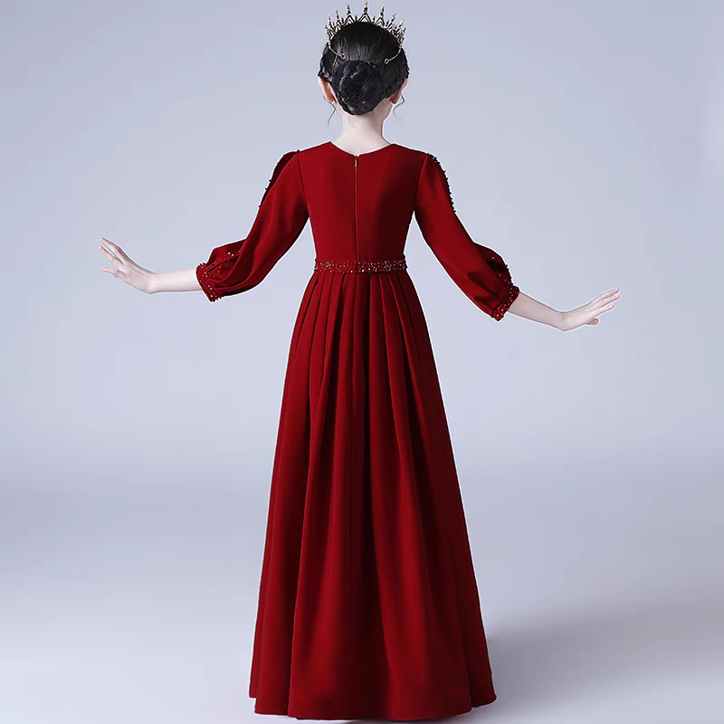 Back view of a girl wearing a long-sleeved, red formal gown with beaded accents and a matching tiara.