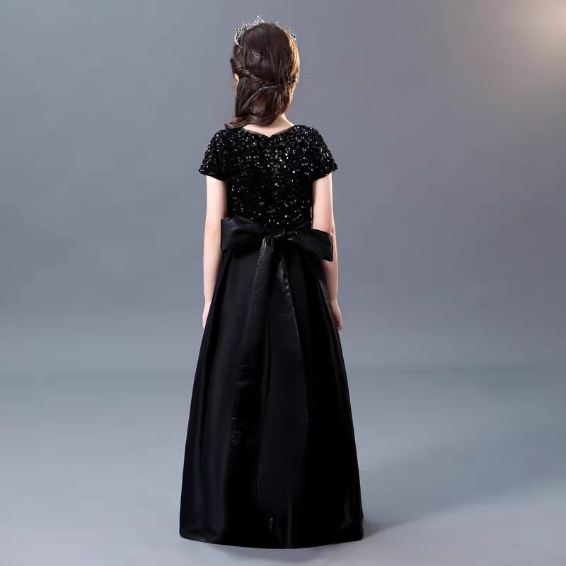 Back view of a girl wearing a black sequin bodice dress with a satin skirt and bow.