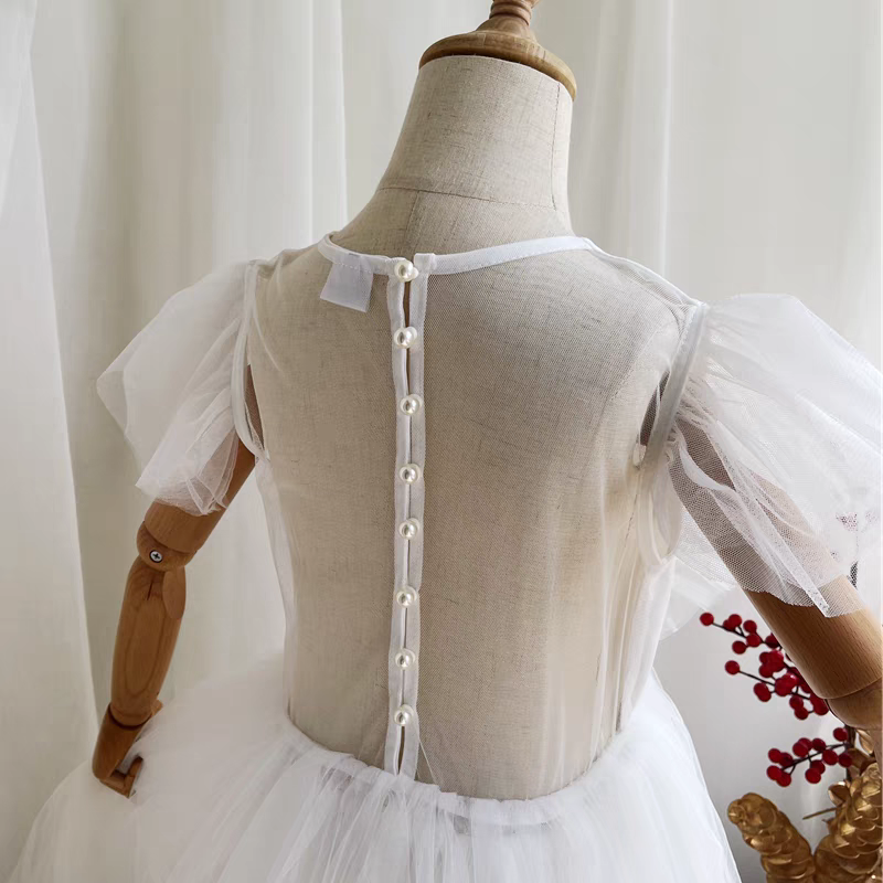 Back view of a white tulle dress with pearl button closure and sheer puff sleeves.