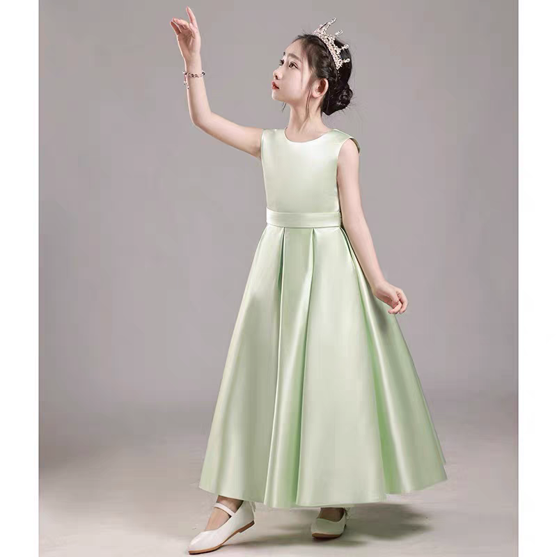 Girl in a light green satin dress with a crown, posing with hand raised.