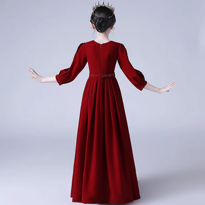 Back view of a girl wearing a long-sleeved, red formal gown with beaded accents and a matching tiara.